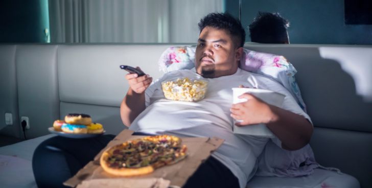 ピザ、ドーナツ、ポップコーンを食べる肥満男性